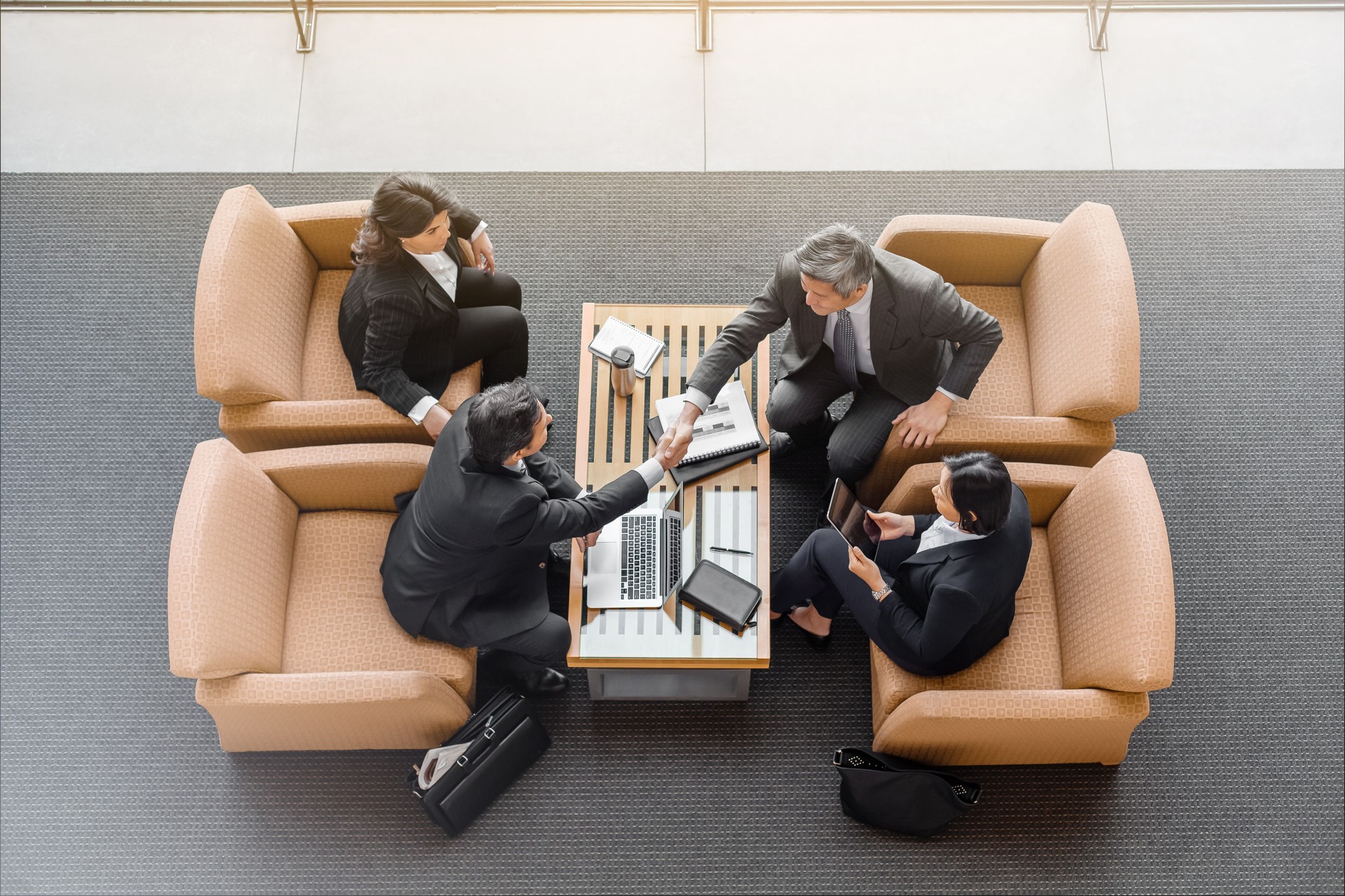 High angle view of business people shaking hands in airport departure area lobby
